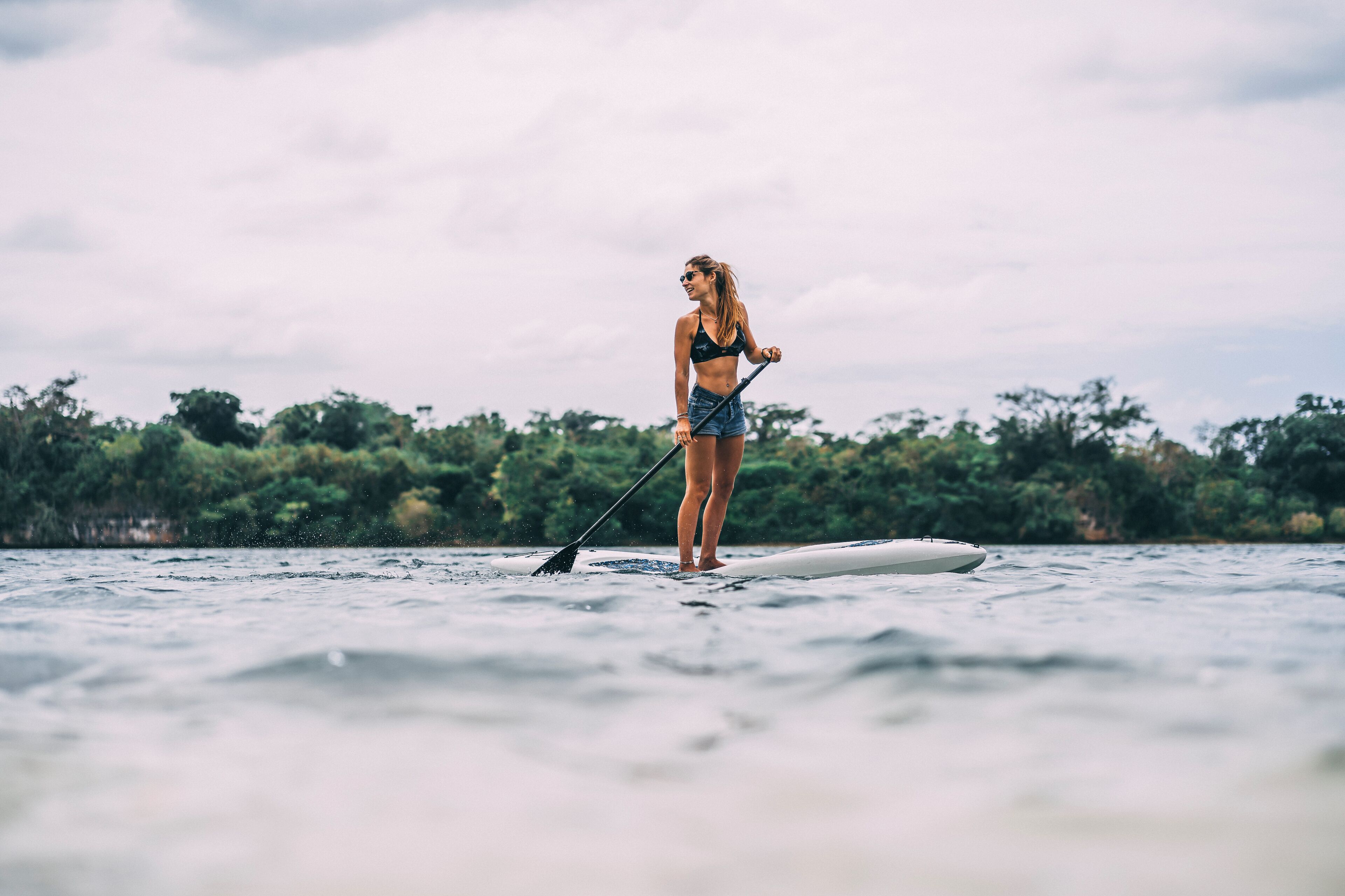A person standing on a paddleboard in a body of water with trees in the background.