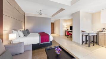 Una habitación de hotel moderna con una cama, un sofá, una mesita de centro con una flor, un escritorio y una zona de cocina.