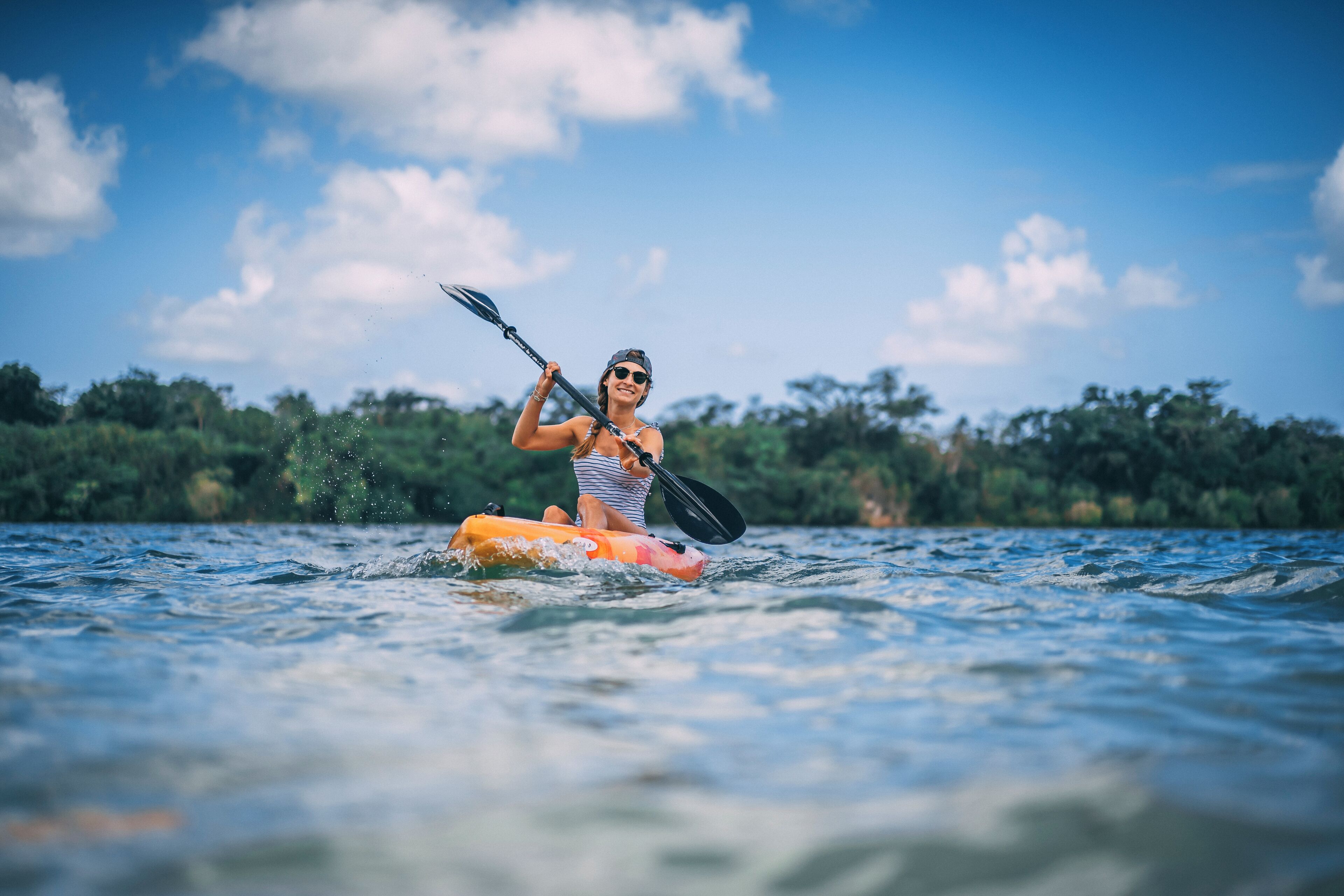 Une personne pratiquant le kayak sur une rivière, avec un ciel dégagé et des arbres en arrière-plan.