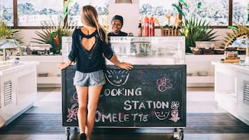 Eine Frau steht an einer Theke, auf der mit 'Cooking Station Omelette' beschriftet ist. Ein Mann steht dahinter.