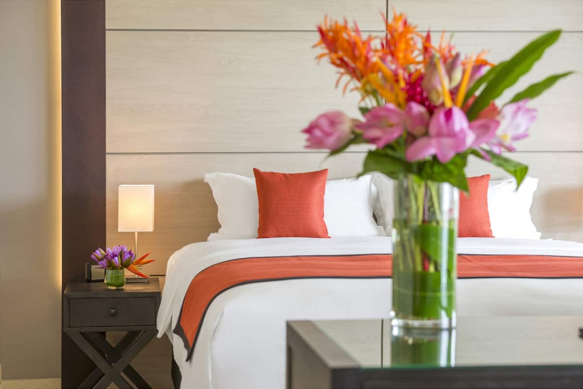 Ein Hotelzimmer mit einem ordentlich bezogenen Bett, einem Nachttisch mit Lampe und einer Blumenvase.
