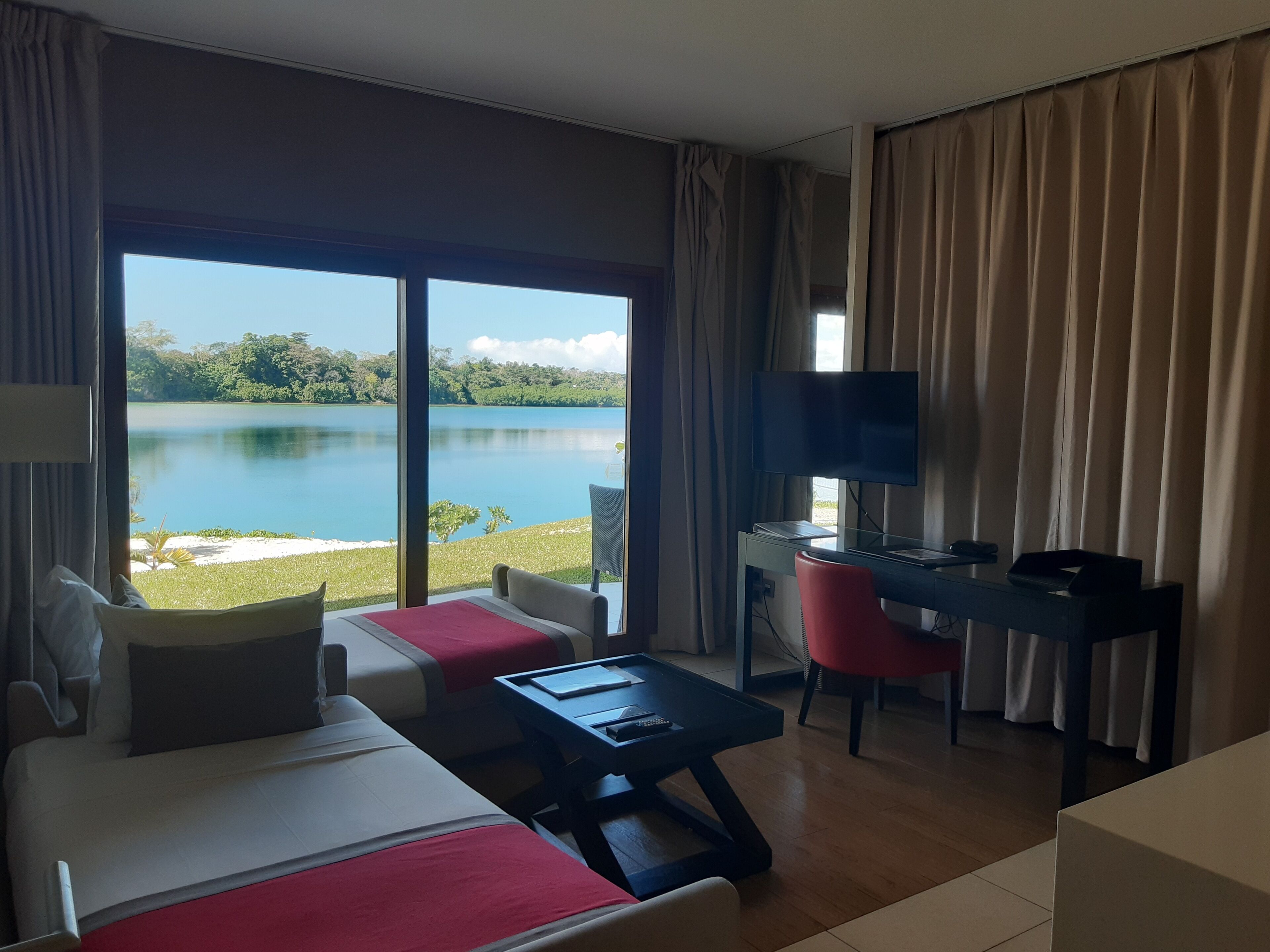 A hotel room with a large window offering a lake view, a bed, a desk with a chair, and a television.