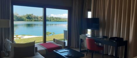 A hotel room with a large window offering a lake view, a bed, a desk with a chair, and a television.