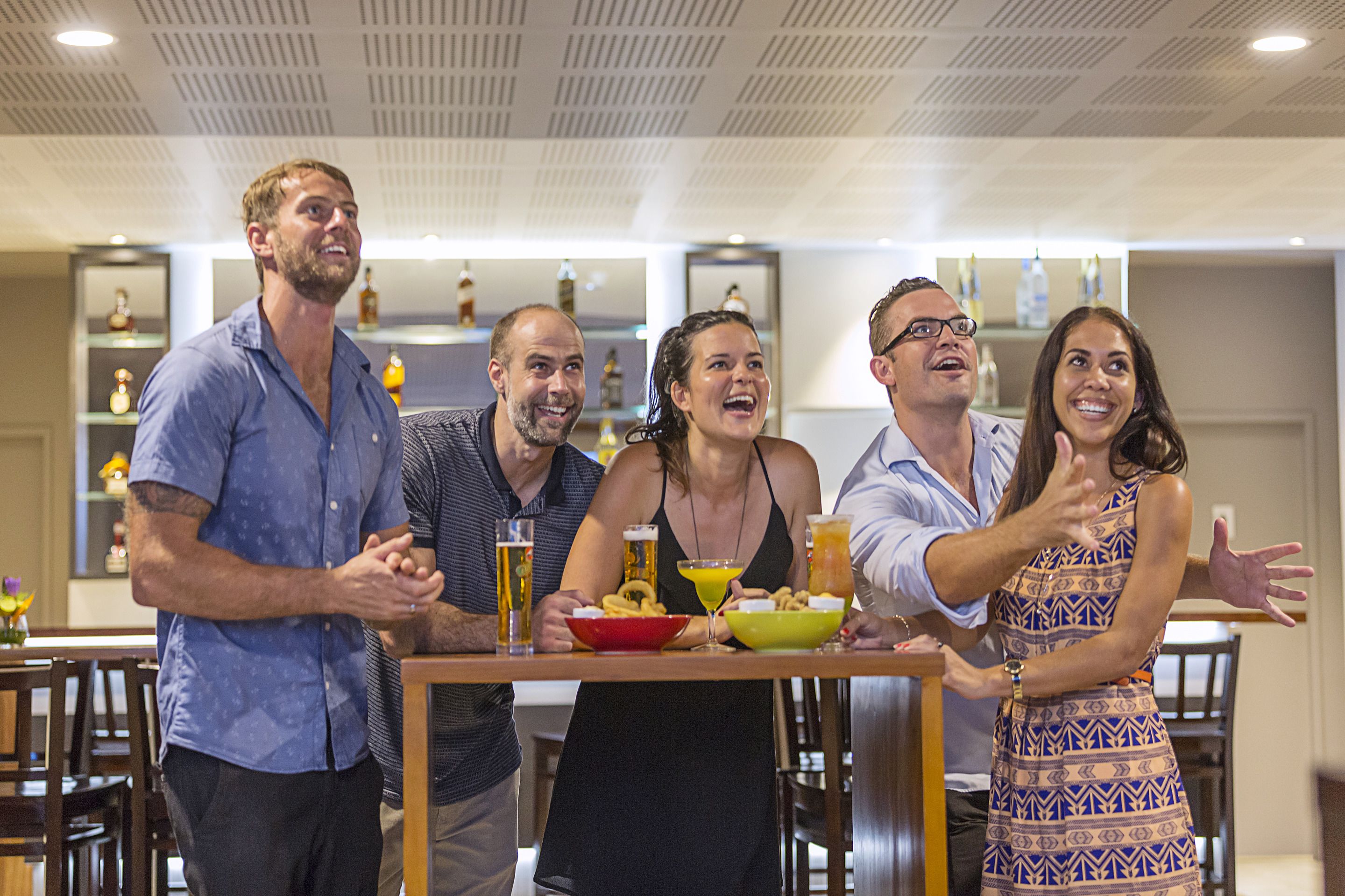 Un grupo de personas de pie alrededor de una mesa con bebidas y aperitivos.