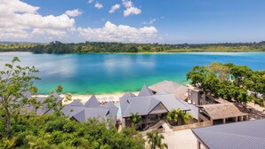 Een resort met meerdere bungalowgebouwen, een strand en een heldere blauwe zee.