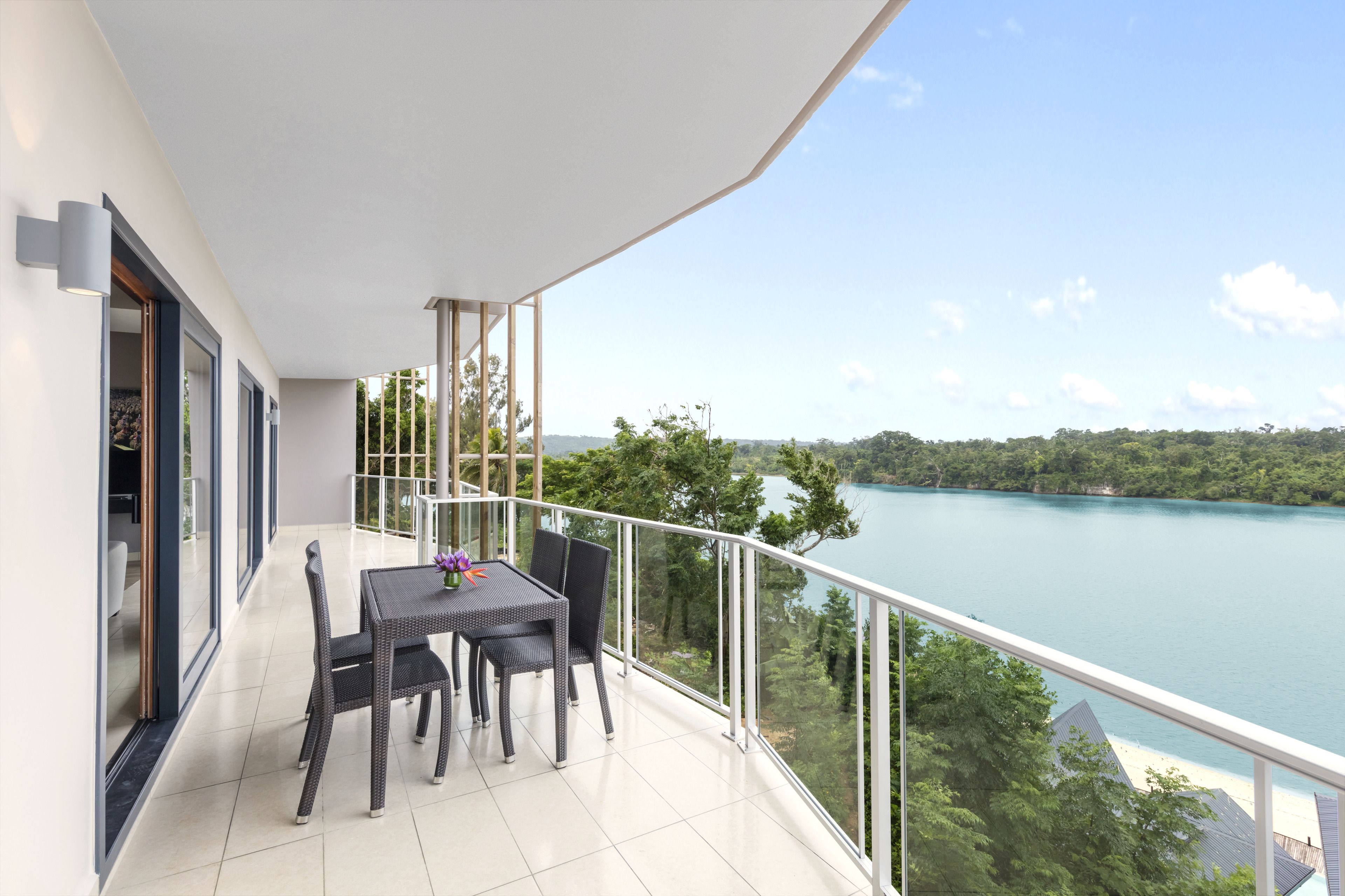 A balcony with a table and chairs, overlooking a lake and forested area.