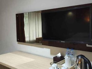 A hotel room with a flat-screen TV mounted on the wall, a wooden counter, and a coffee maker. - Ramayana Tasik (Tasikmalaya)