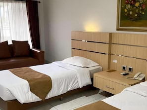 Ett hotellrum med en säng, ett nattduksbord med en telefon, ett litet skåp och en soffa.