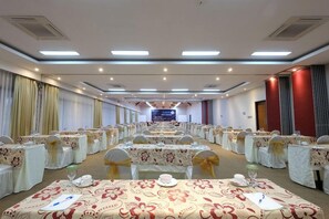 A conference room with rows of tables, each with a floral tablecloth and gold sashes, equipped with chairs and water bottles. - Rumah Kito Jambi (Jambi)
