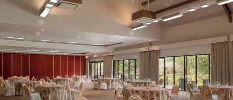 A banquet hall with round tables, white chairs, and a red wall.