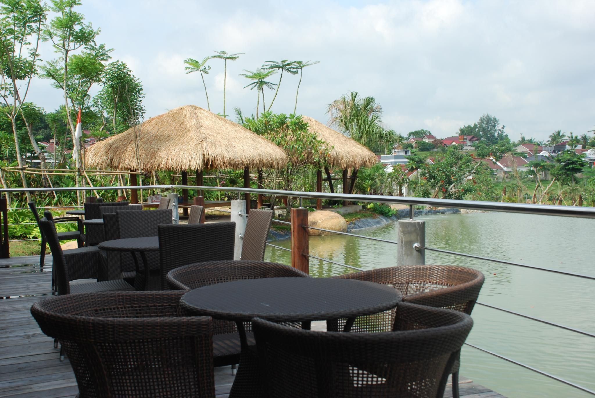 Une terrasse dotée de meubles en osier et de parasols en chaume, offrant une vue sur une étendue d’eau.