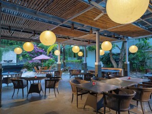 An outdoor dining area with wicker furniture, hanging spherical lights, and a view of a garden with tropical plants. - Rumah Kito Jambi (Jambi)