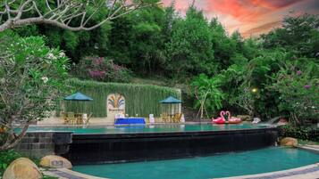 A pool area with a waterfall feature, surrounded by lush greenery and a stone wall with a sign.