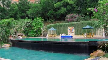 A swimming pool with a waterfall feature, surrounded by lush greenery and a stone wall with a mural.