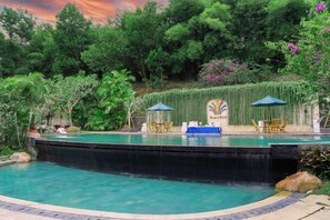A swimming pool with a waterfall feature, surrounded by lush greenery and a stone wall with a mural. - Rumah Kito Jambi (Jambi)