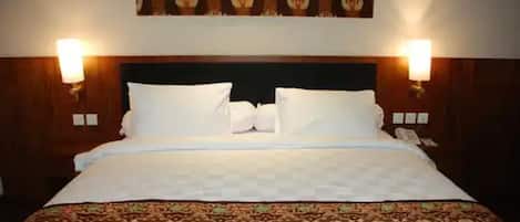 A hotel room with a large bed, two bedside lamps, a patterned headboard, and a floral wall hanging.