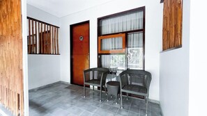 A room with a door, two wicker chairs, a table, and a window with curtains. - Rumah Kito Jambi (Jambi)