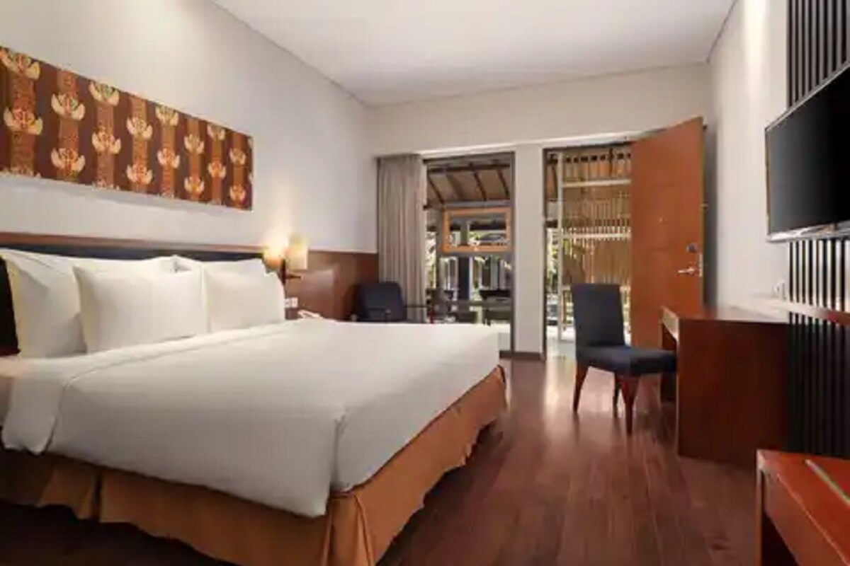A hotel room with a large bed, a desk, a chair, a TV, and a wardrobe.