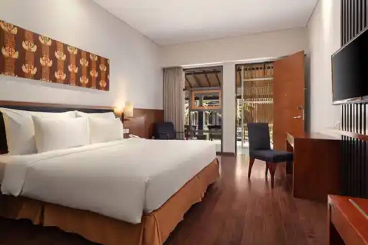 Quarto de hotel com uma cama grande, uma escrivaninha, uma cadeira, uma televisão e um guarda-roupa.