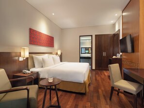 Une chambre d’hôtel avec un lit, des tables de chevet, un bureau, une chaise, une télévision et une salle de bain visible à travers une porte ouverte.