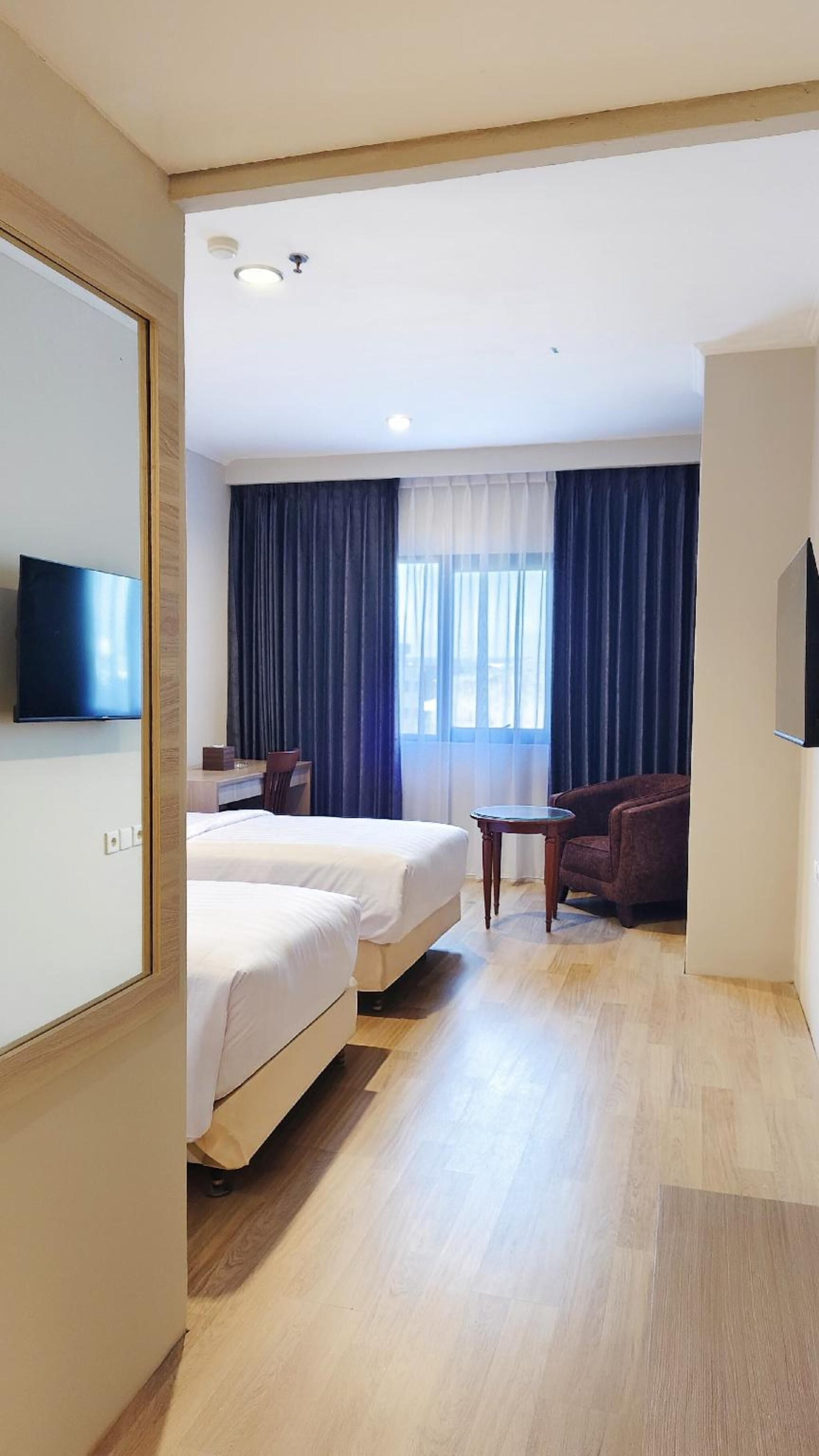 Hotellihuone, jossa on kaksi sänkyä, televisio, työpöytä ja tuoli.