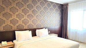 A hotel room with a large bed, a nightstand with a phone, and a patterned wallpaper. - Royal Asia Palembang (Palembang)