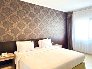 A hotel room with a large bed, a nightstand with a phone, and a patterned wallpaper.