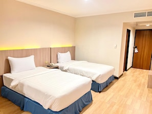 Ein Hotelzimmer mit zwei Betten, einem hölzernen Kopfteil, einem Nachttisch mit Telefon und einer Tür zu einem weiteren Raum.