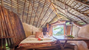 A room with a bed, a wooden table, and a view of greenery outside. - Vanira Lodge (Taiarapu-Ouest)