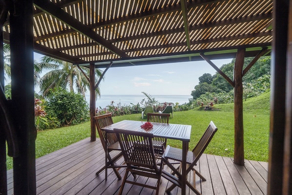 Una terraza de madera con una mesa y sillas, con vistas a un jardín exuberante y al mar.