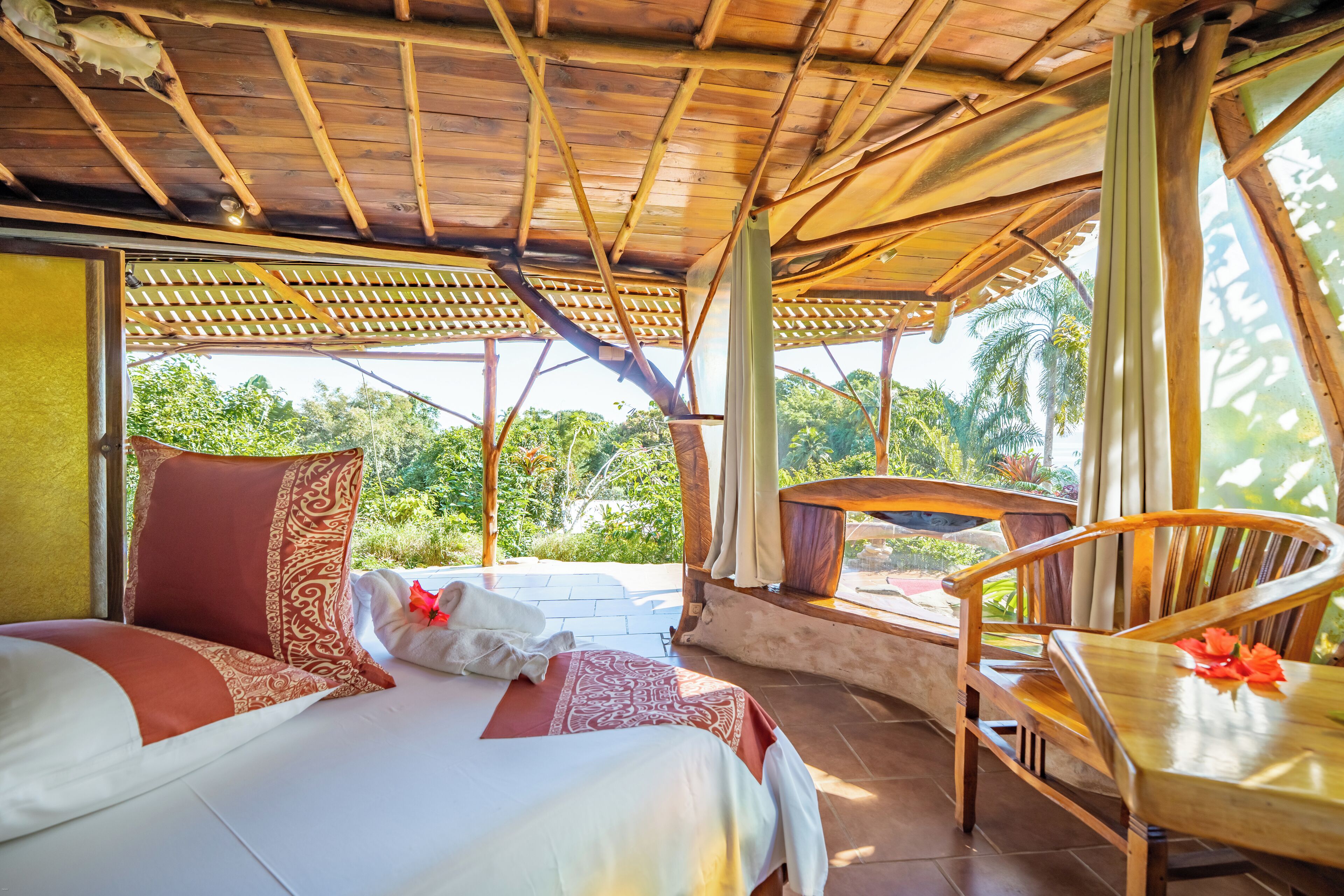A room with a bed, a wooden chair, and a view of greenery outside.