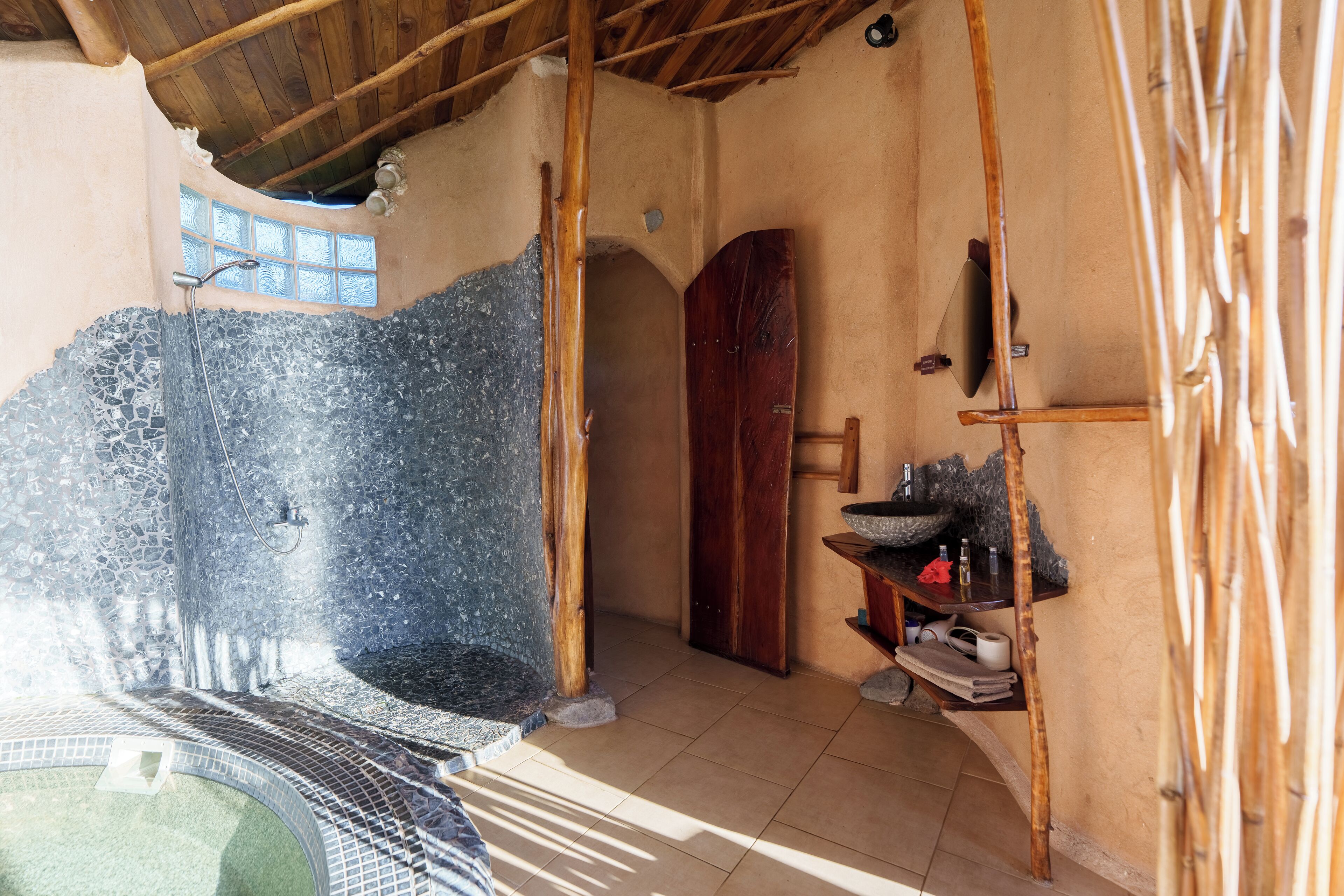 A spa area with a stone hot tub, wooden door, and shelves with toiletries.