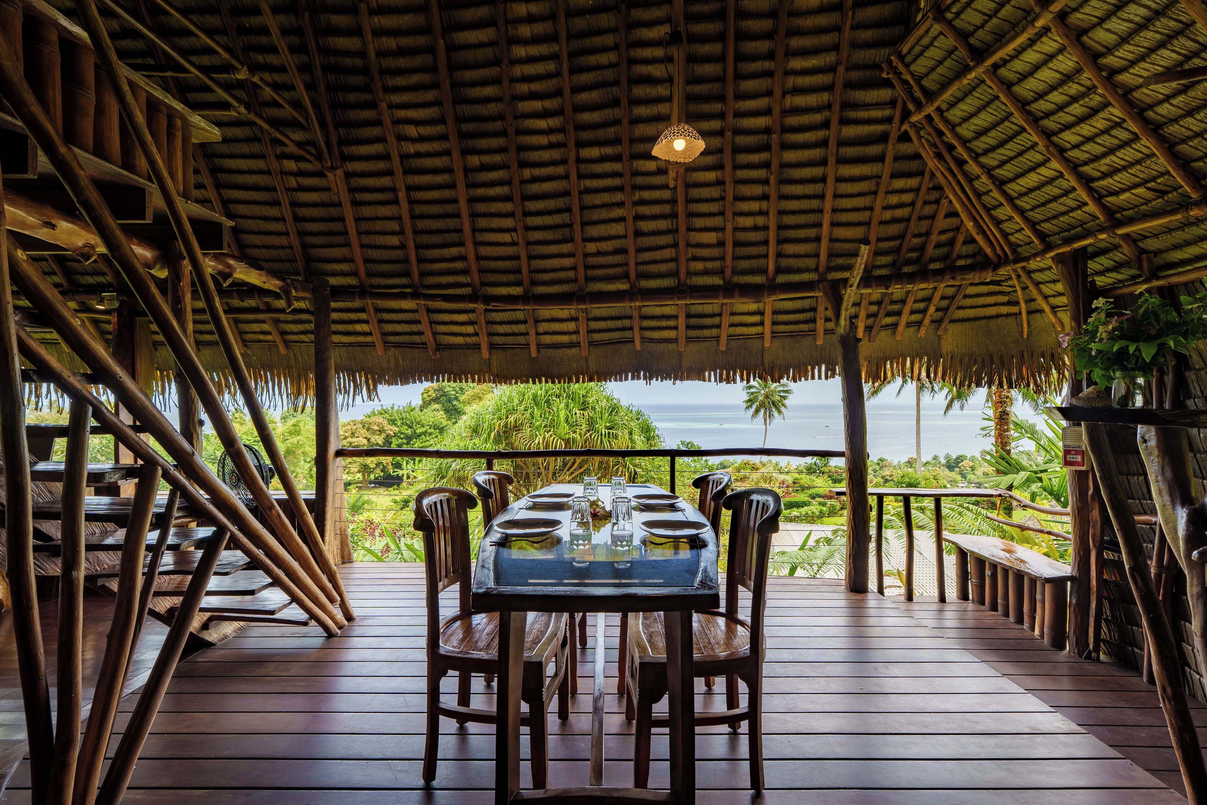 An outdoor dining area with a thatched roof, wooden furniture, and a view of the ocean.