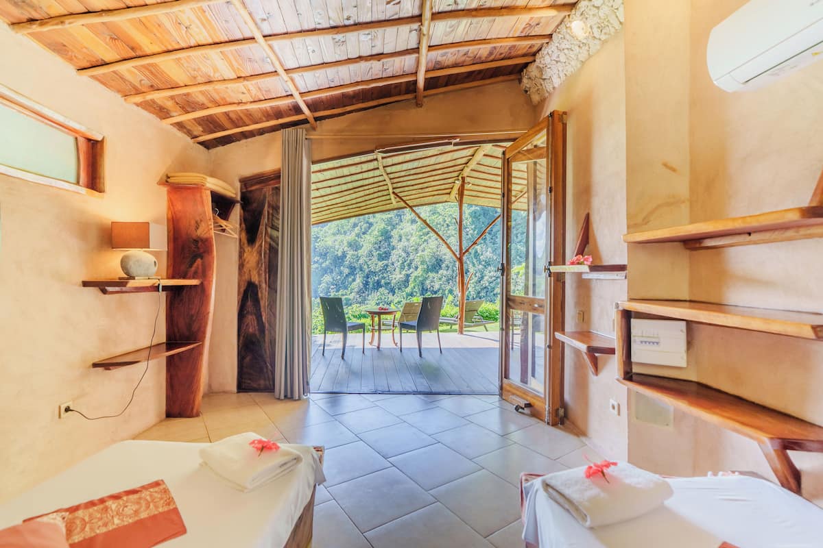 Une chambre avec deux lits, un plafond en bois, une vue sur un jardin et une porte donnant sur l’extérieur.