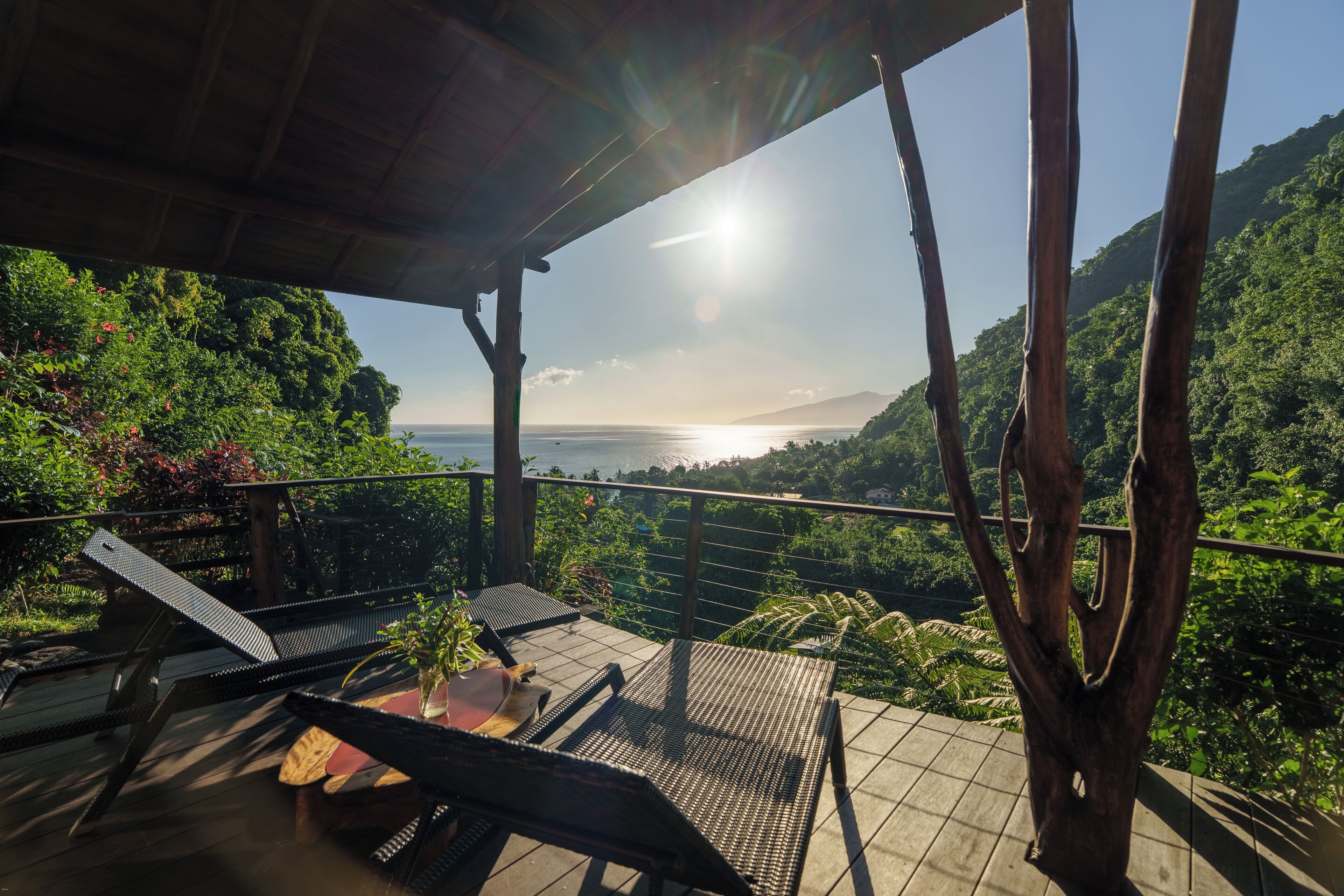 Eine Terrasse mit Liegestühlen und einem Tisch, mit Blick auf eine üppige Landschaft und das Meer.