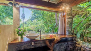 A bathroom with a stone sink, wooden countertop, and a view of lush greenery outside. - Vanira Lodge (Taiarapu-Ouest)