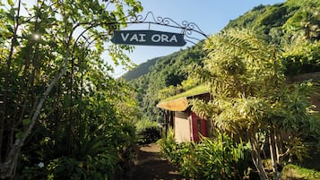 A sign reading "VAI ORA" in a lush, green environment with a path leading to a small building.