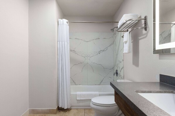 A modern bathroom with a marble shower wall, a bathtub, a toilet, and a sink with a towel rack.