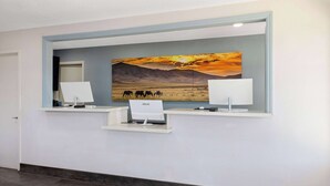 Un área de recepción con un escritorio, una computadora y un cuadro de un paisaje.