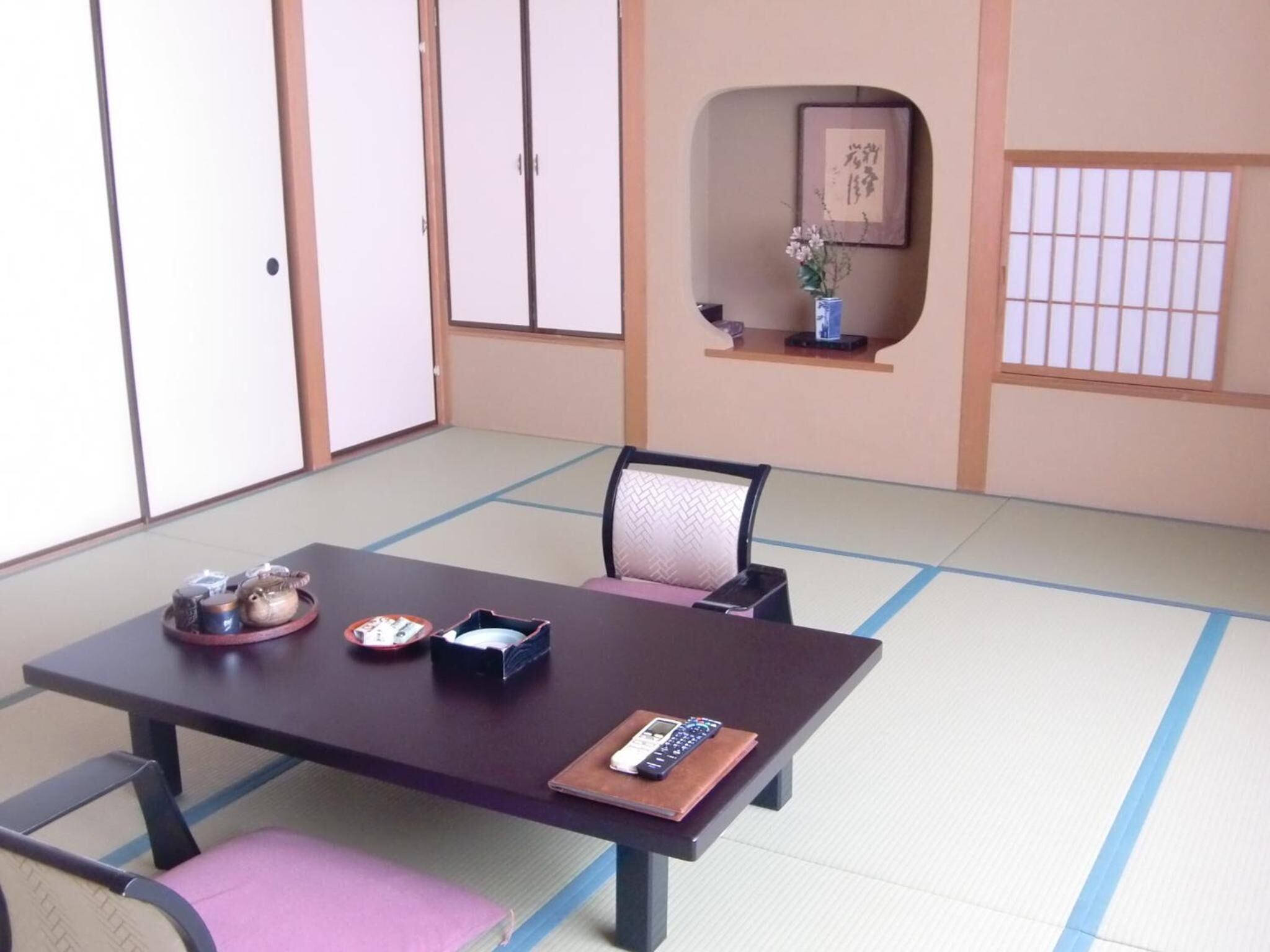 Um quarto japonês tradicional com esteiras de tatame, uma mesa baixa, cadeiras e uma porta deslizante.