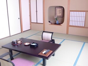 Una habitación tradicional japonesa con tatami, una mesa baja, sillas y una puerta corredera.