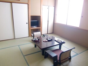 Una habitación japonesa tradicional con suelo de tatami, una mesa baja con banco, un televisor en un estante y puertas correderas.