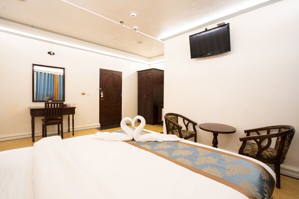 A hotel room with a large bed, a desk, two chairs, a television, and a door.