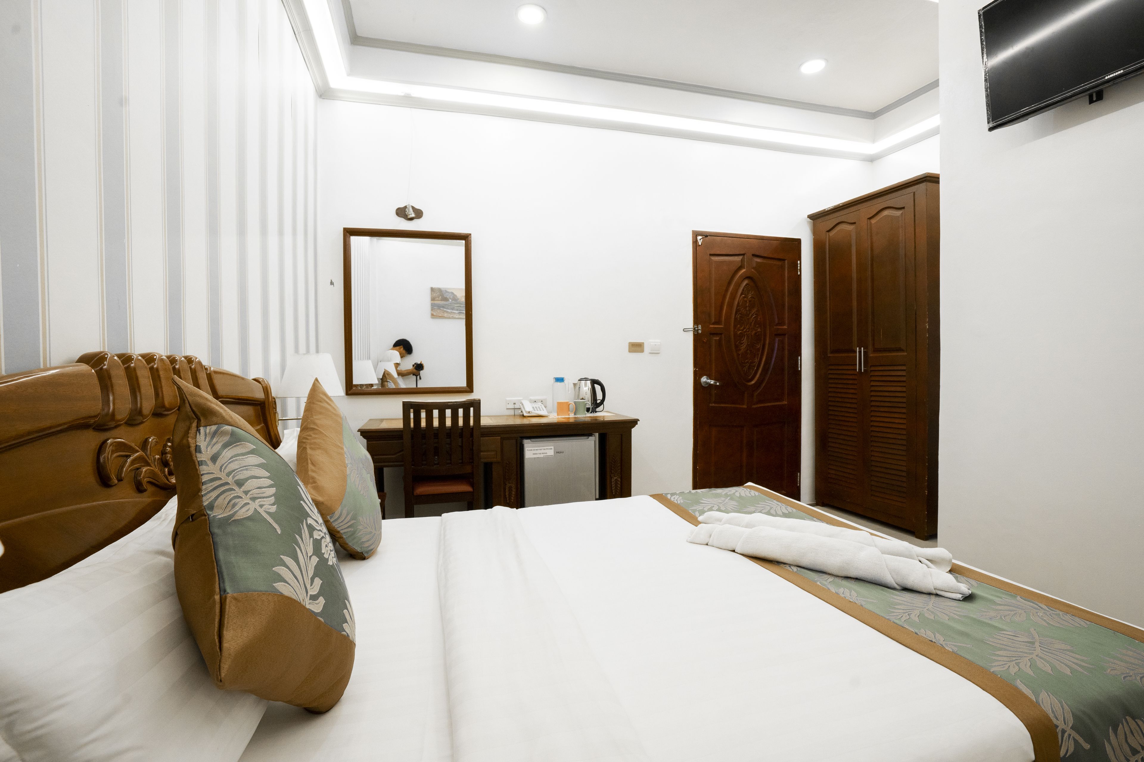 A hotel room with a bed, a desk, a mirror, and a wardrobe.