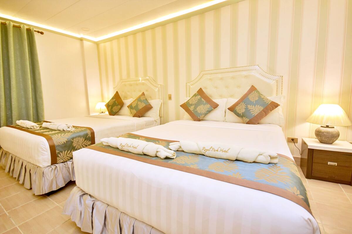 Quarto de hotel com duas camas, papel de parede listrado e cortina verde.