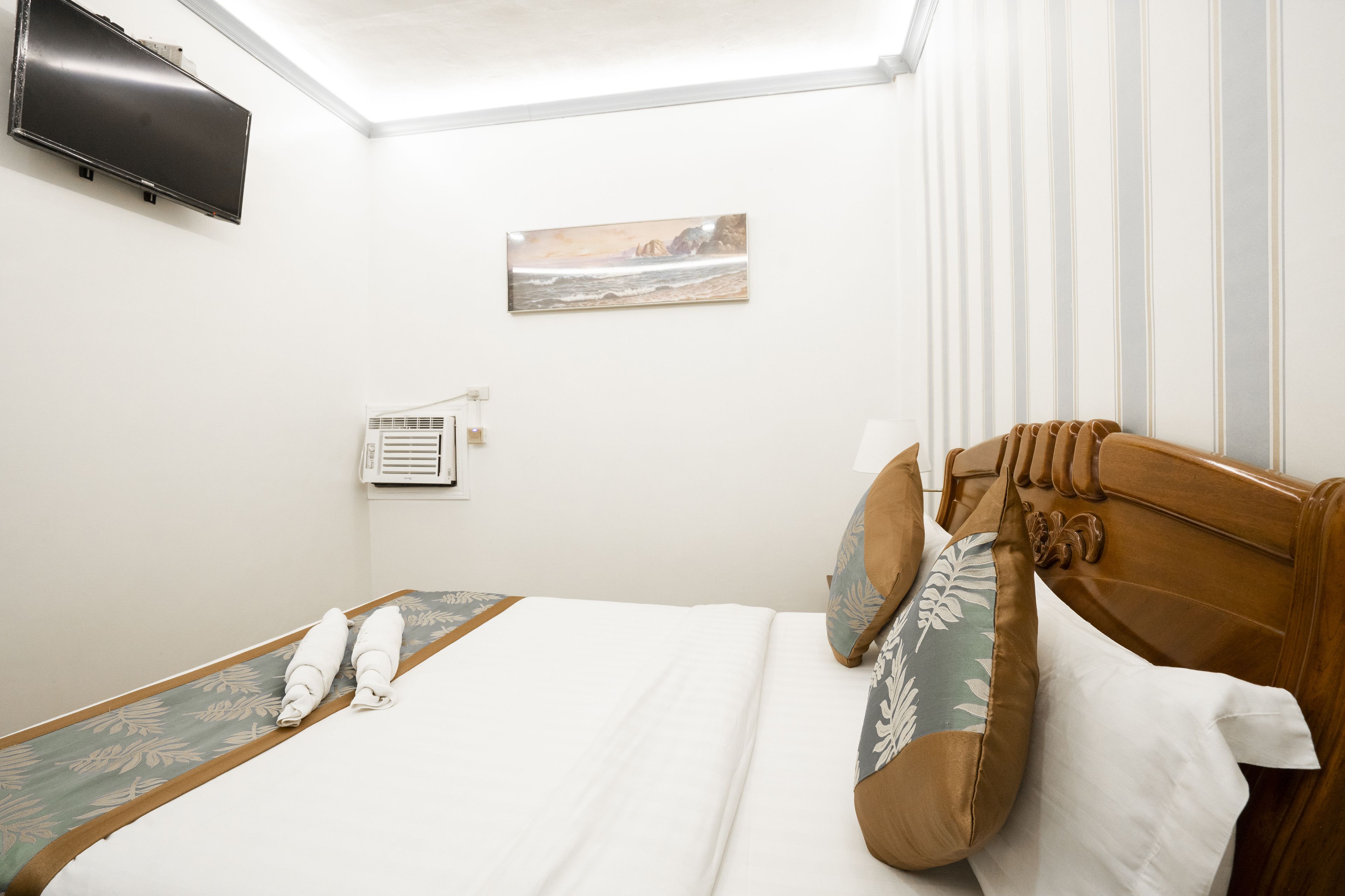 Une chambre d’hôtel équipée d’un lit, d’un téléviseur à écran plat fixé au mur, d’un climatiseur et d’un tableau représentant une scène de plage.