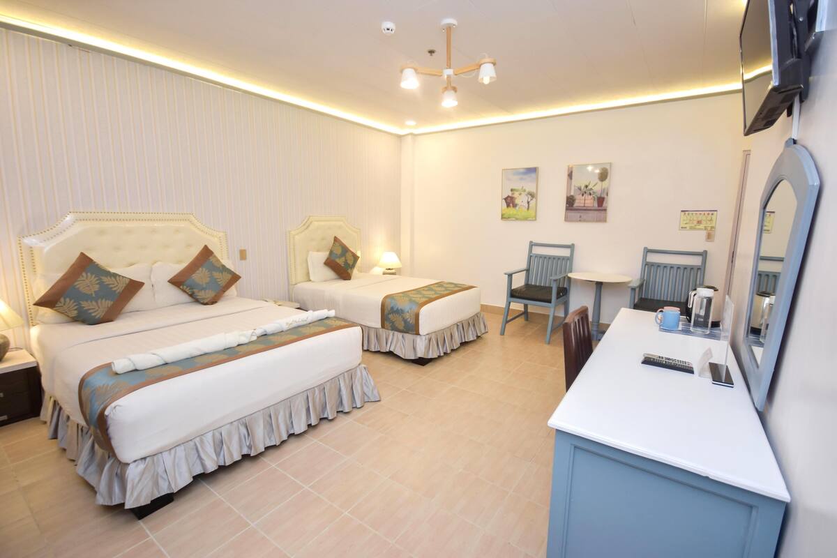 Quarto de hotel com duas camas, uma escrivaninha e uma cadeira.