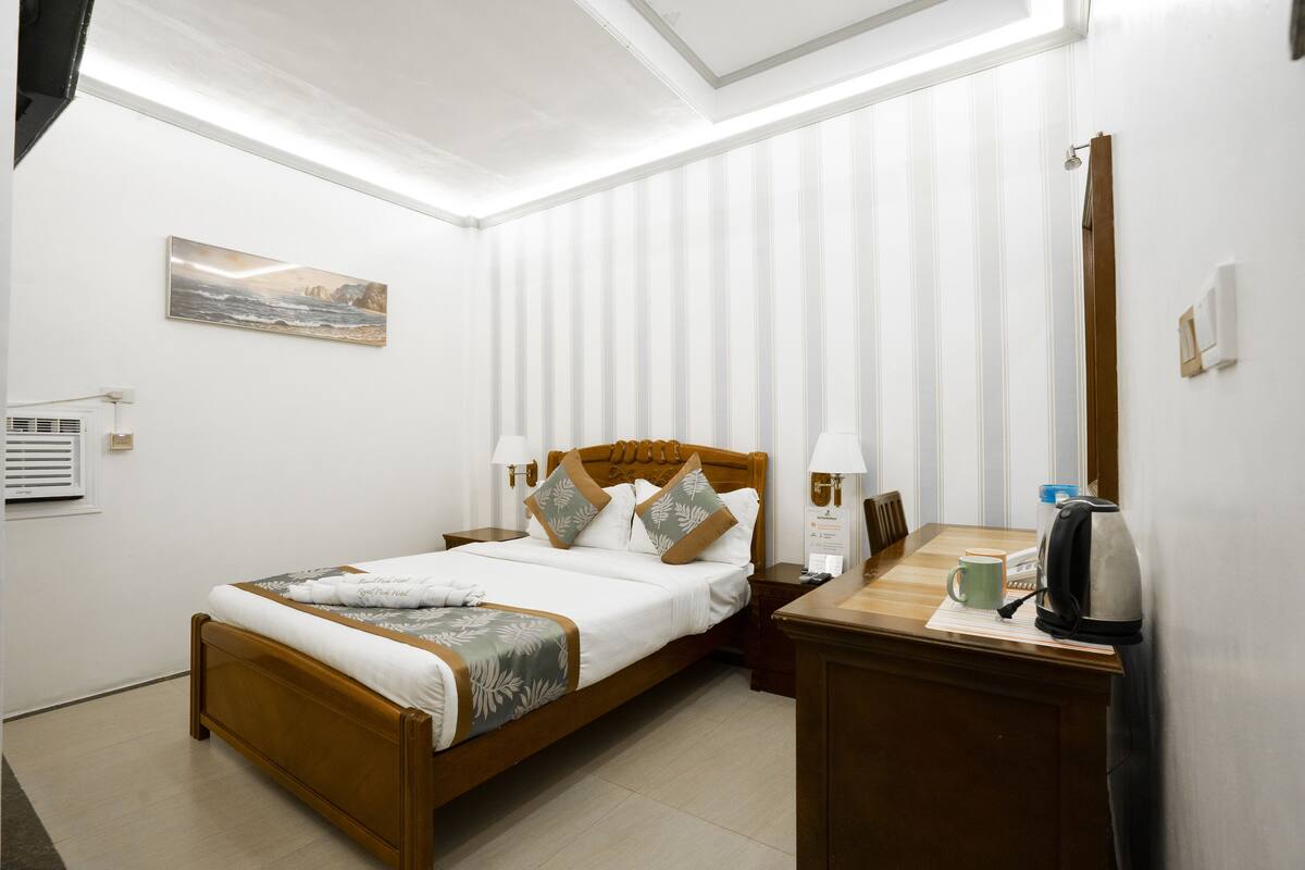 Quarto bem arrumado com cama de madeira, mesas de cabeceira, um criado-mudo, cafeteira e um quadro na parede.
