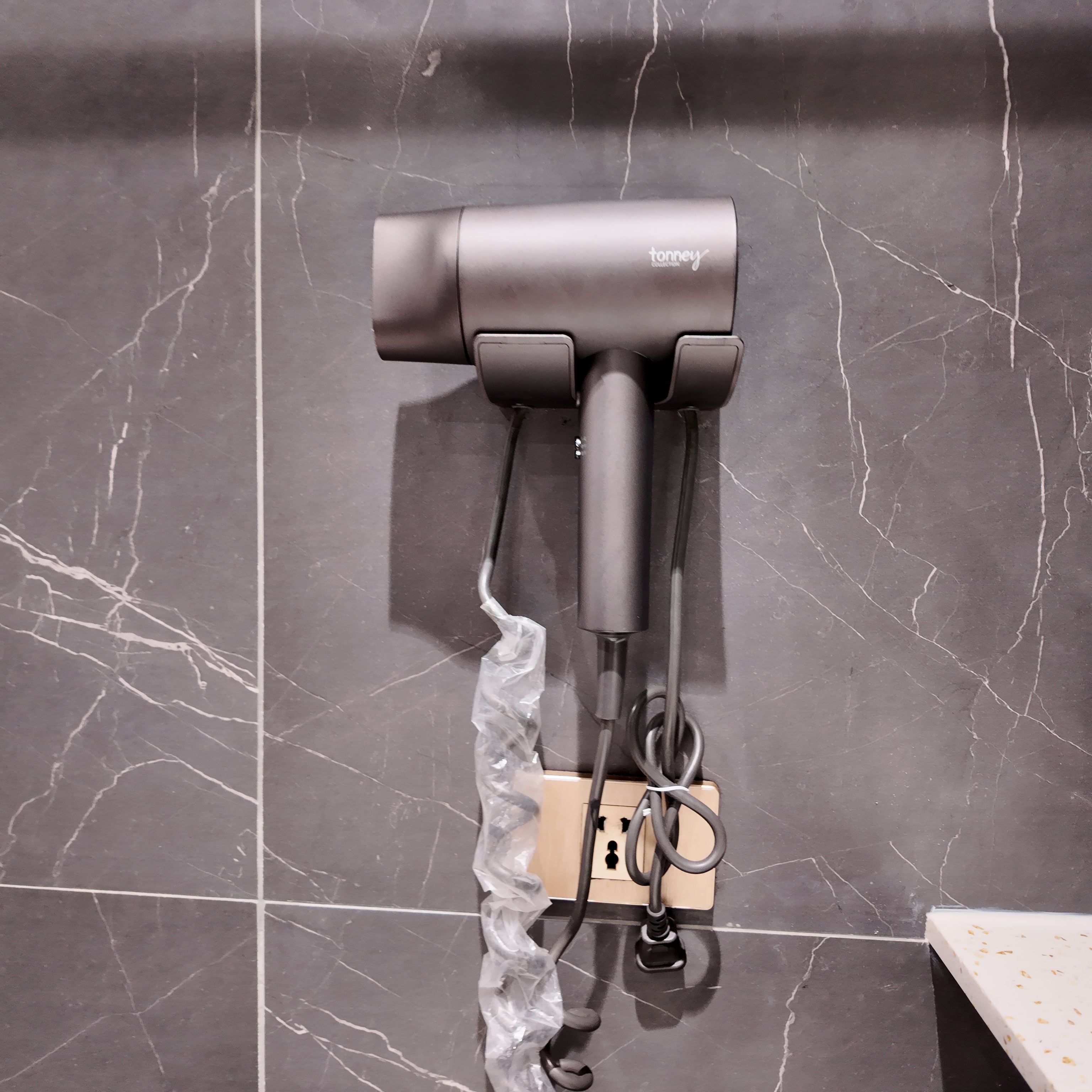 Un secador de pelo sujeto a la pared, con un enchufe debajo.
