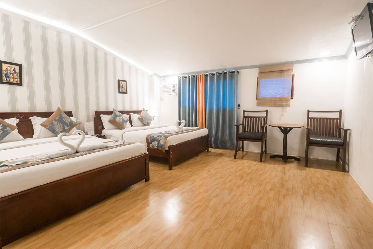 Quarto de hotel com duas camas, uma mesinha e uma cadeira.